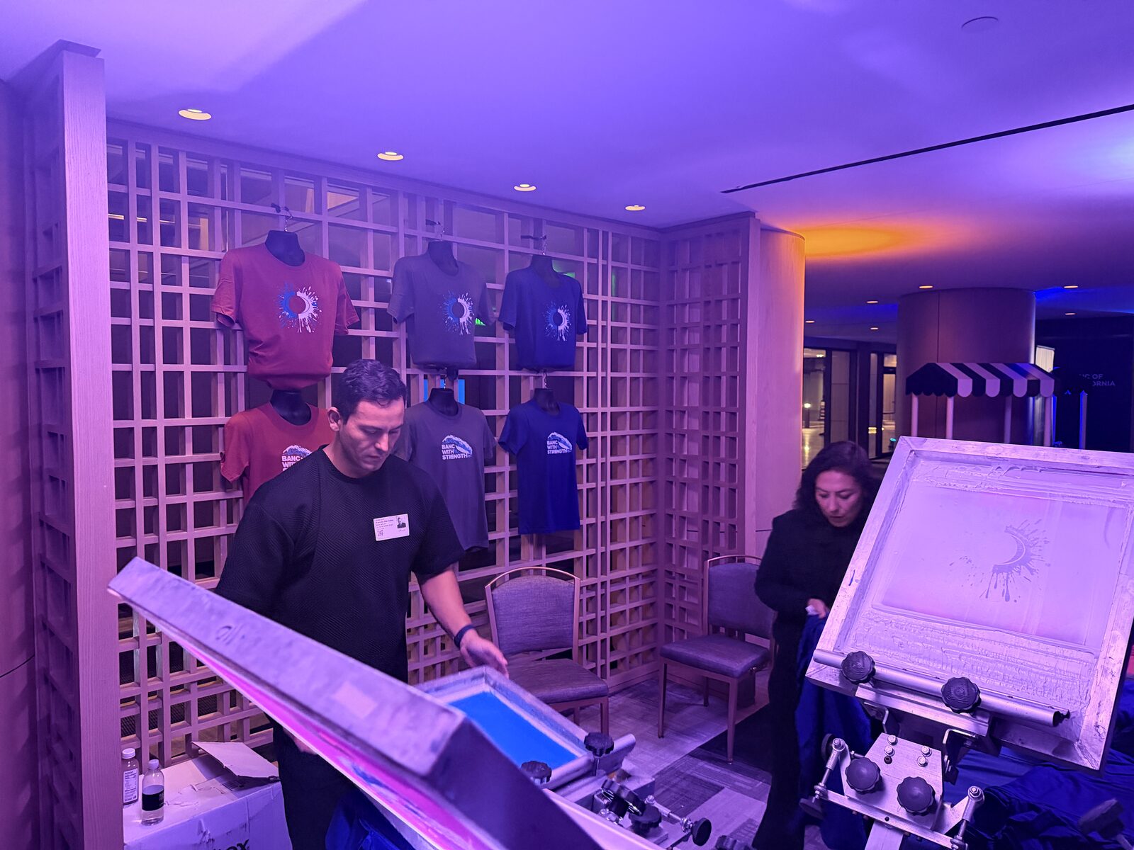 Wall of custom event shirts hung behind a printing station
