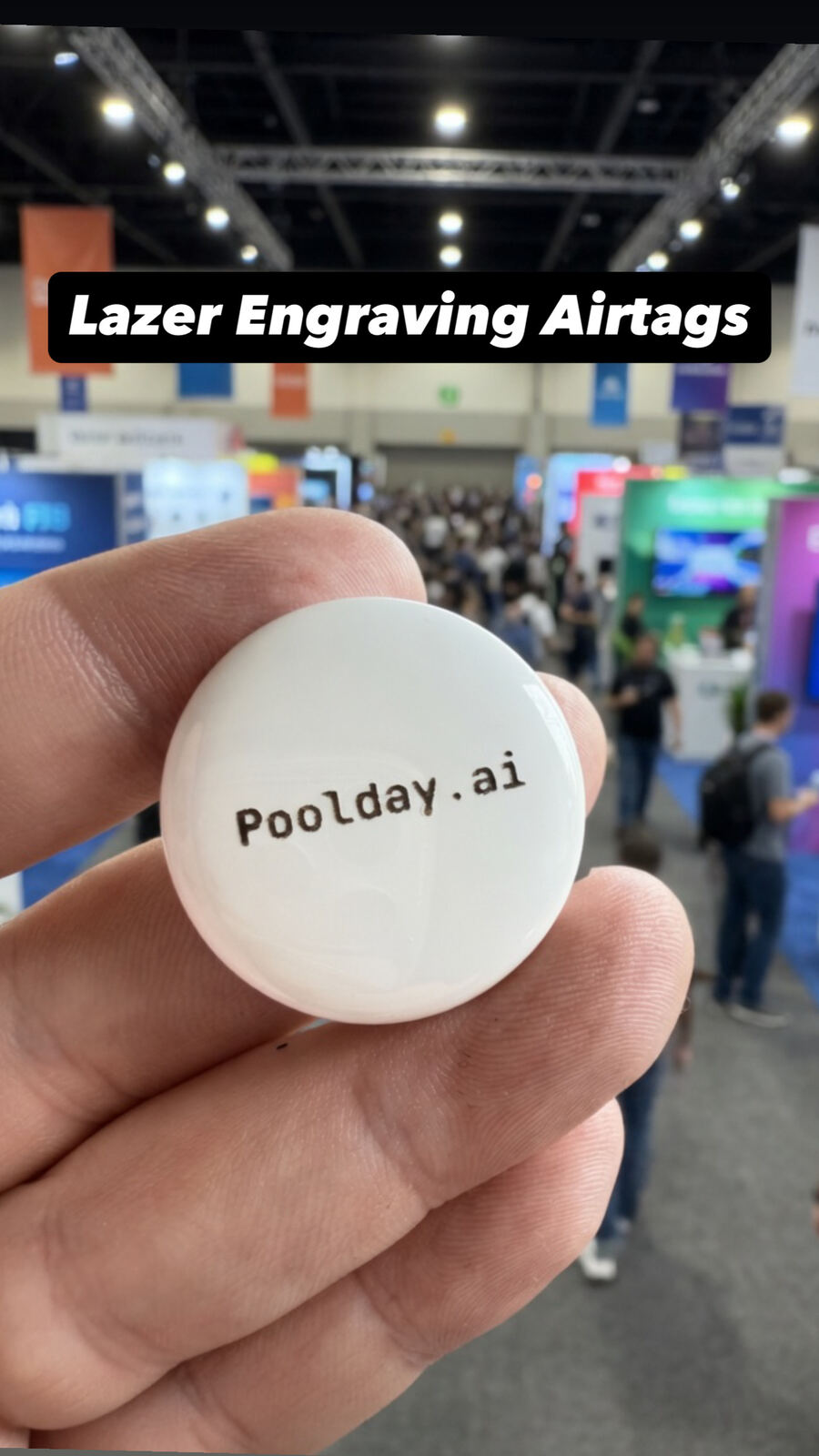 Attendee holding a white laser-engraved circular AirTag pendant at a booth
